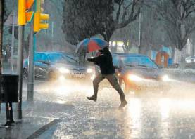 Una persona creua un carrer enmig d’una tromba d’aigua. Foto: DT