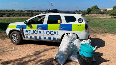 El coche patrulla y las algarrobas recuperadas. FOTO: Policia Local de Vila-seca