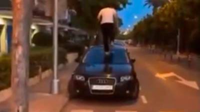 Frame del vídeo de un jóven subido al capó de un BMW negro.