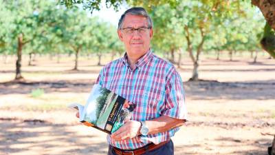 Joan Tous posa con un ejemplar de su libro en una finca de algarrobos de Vila-seca. Foto: Alba MAriné