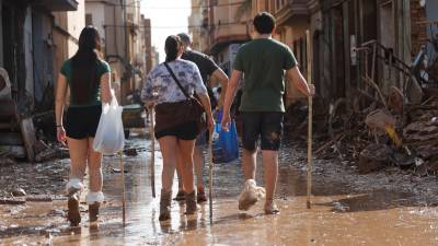 Varias personas caminan entre el lodo acumulado en las calles a causa de las intensas lluvias caídas por la fuerte dana, este jueves en Catarroja. Catarroja, una de las localidades afectadas por la dana que asoló este martes la provincia de Valencia, se afana por restablecer los suministros cortados a consecuencia del temporal y en ofrecer ayuda humanitaria a los vecinos. Foto: EFE