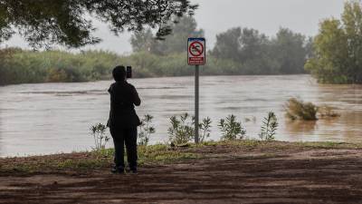 Una mujer toma imágenes del gran caudal del rió Júcar a su paso por Albalat de la Ribera a causa de la dana que ha afectado a la provincia de Valencia. Foto: EFE