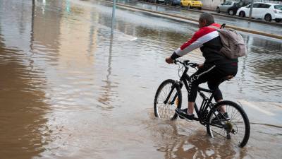 Una persona en bicicleta con la calle inundada. Foto: EFE