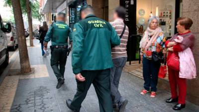 Dos agentes de la Guardia Civil saliendo con un detenido de uno de los registros realizados durante el operativo. Foto: ACN