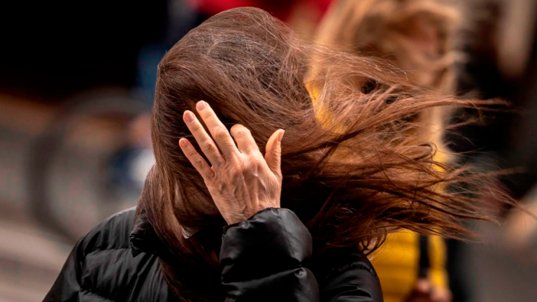 Una mujer intenta quitarse el cabello de la cara empujado por el viento. Foto: EFE