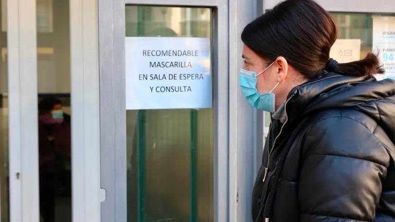 Una mujer con mascarilla observa un cartel en el que se recomienda el uso de mascarilla dentro de un centro sanitario. Foto: EFE