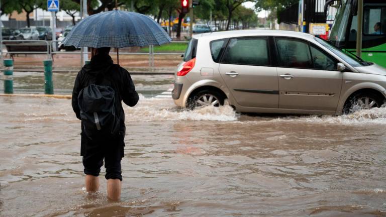 Un hombre bajo su paraguas y un coche intentando circular con una intensa lluvia. Foto: EFE