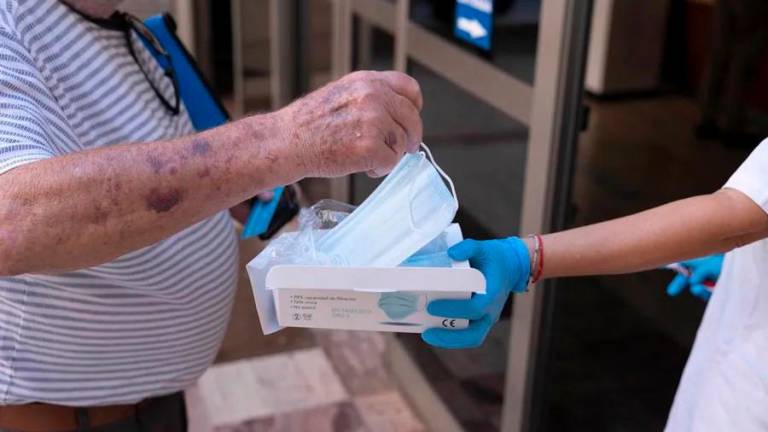 Una trabajadora de un centro de salud entrega una mascarilla a un paciente. Foto: EFE