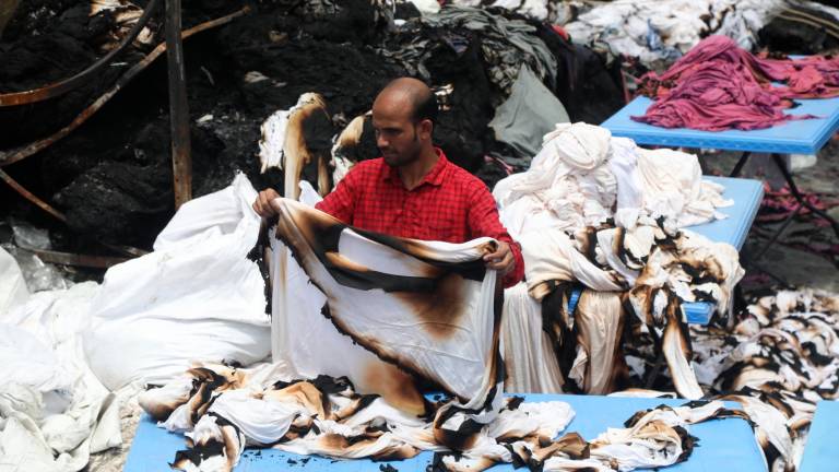 Un trabajador textil en la capital de Bangladés, Daca, intenta salvar tejidos tras el incendio de la factoría por los disturbios, en julio. Foto: Monirul Alam/EFE