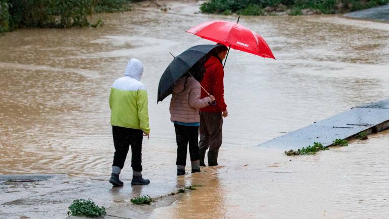 Varias personas intentan cruzar el cauce de la Rambla del Garruchal inundado a causa de la intensas lluvias caídas este miércoles, en las últimas horas en la pedanía murciana de Beniajan. Foto: EFE