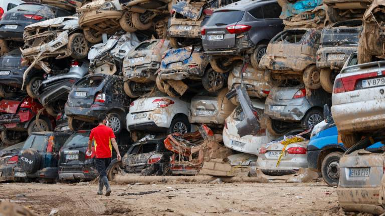 Un voluntario camina junto a una pila de vehículos destrozados en Paiporta, este pasado martes. Foto: EFE