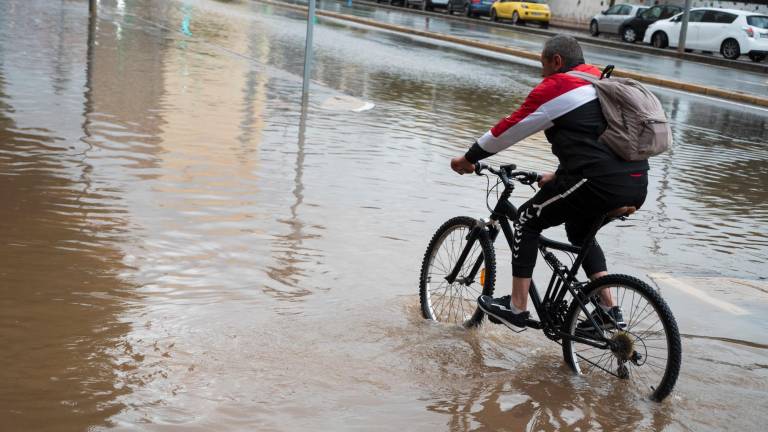 Una persona en bicicleta con la calle inundada. Foto: EFE