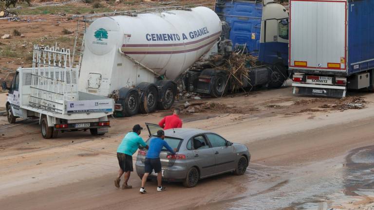 Tres hombres empujan un coche averiado en el polígono industrial de Riba-roja de Túria, este viernes. Foto: EFE