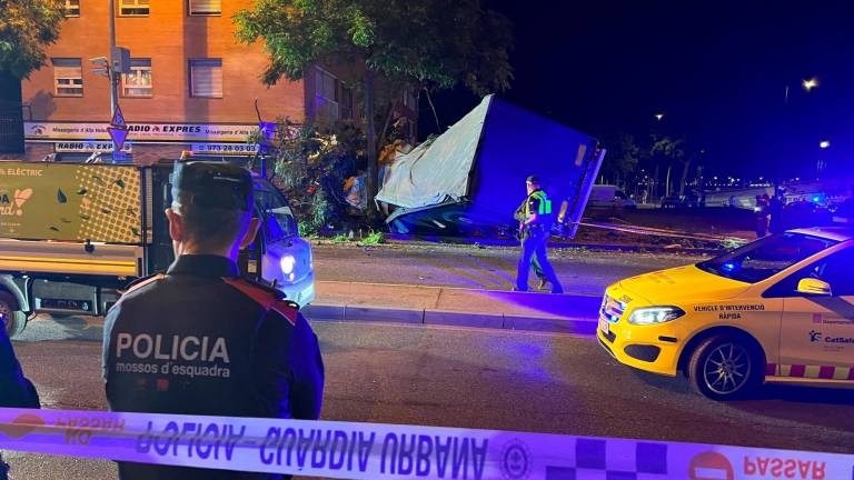 El camión y el tráiler volcados frente al edificio y servicios de emergencia y Mossos en la zona trabajando. Foto: ACN