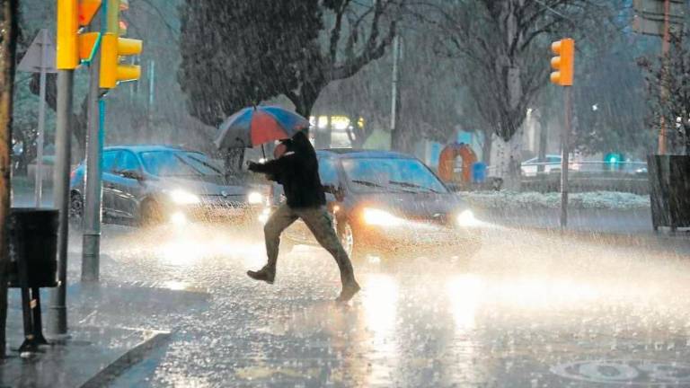 Una persona creua un carrer enmig d’una tromba d’aigua. Foto: DT