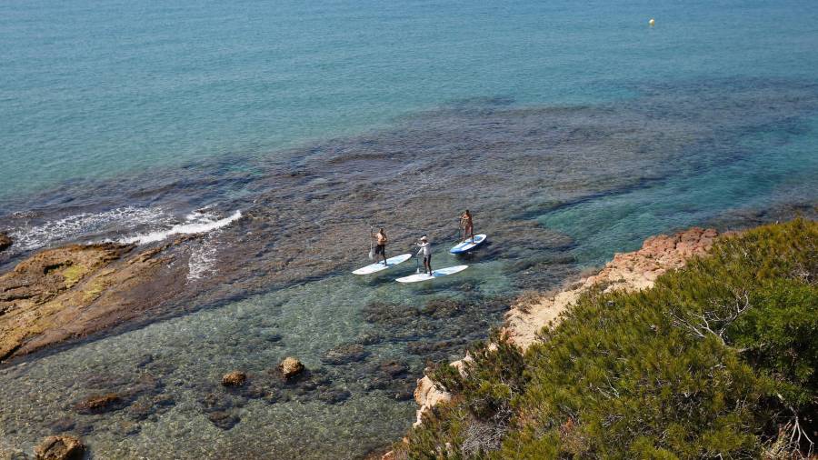 Tres turistas entran con sus tablas en la Roca Plana. Hace 2.000 años por este mismo canal entraba la barcaza para cargar piedra de la cantera del Mèdol.